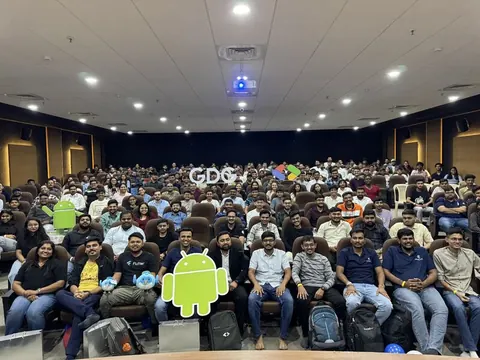 Large audience seated in an auditorium at a GDG Devfest event, with Android cutouts in the foreground.