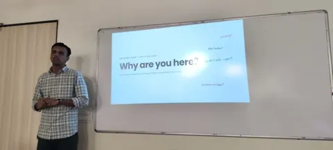 Gaurav stands beside a projected “Why are you here?” slide during an audience-engagement talk.